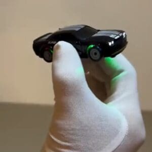 A hand holding a mini miniature black muscle rc drift car toy with double white stripes, glowing headlights, and vibrant green under-glow light illumination.