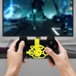 lose-up view of gamer hands holding a black PlayStation 4 controller with a yellow gear-based mini steering wheel attachment installed over the thumbstick for racing games.