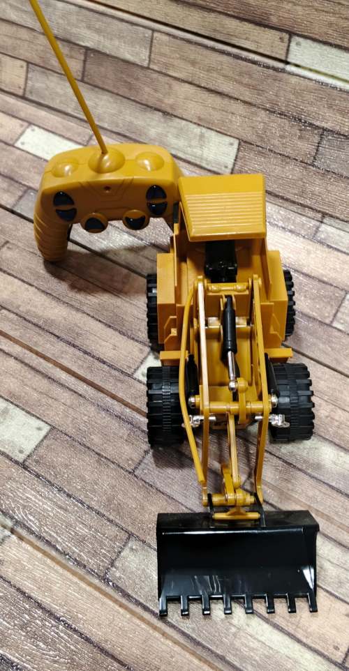 RC Bulldozer construction loader truck remote control toy for kids buy online Beirut Lebanon High-angle view of a yellow remote-controlled toy construction loader truck with a black front scoop bucket beside its yellow remote control